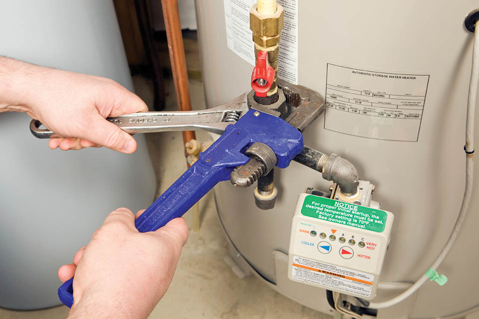 Close-up of an HVAC technician using a monkey wrench on a storage tank water heater
